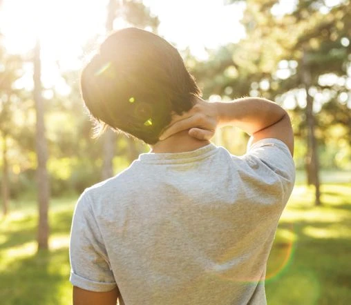 rear view of man in grey shirt touching his neck under the sun