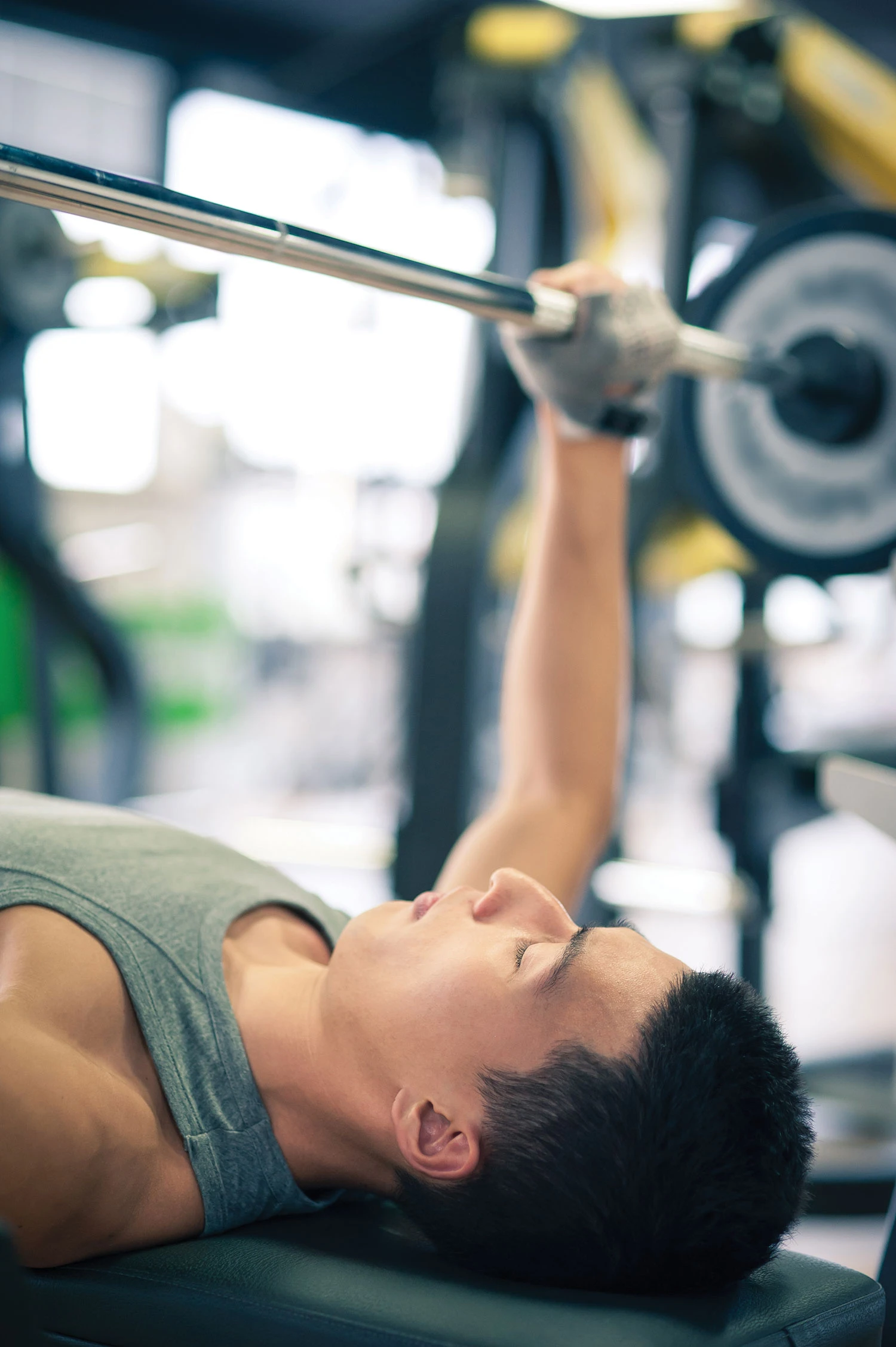 man in grey singlet doing close grip bench press in gym