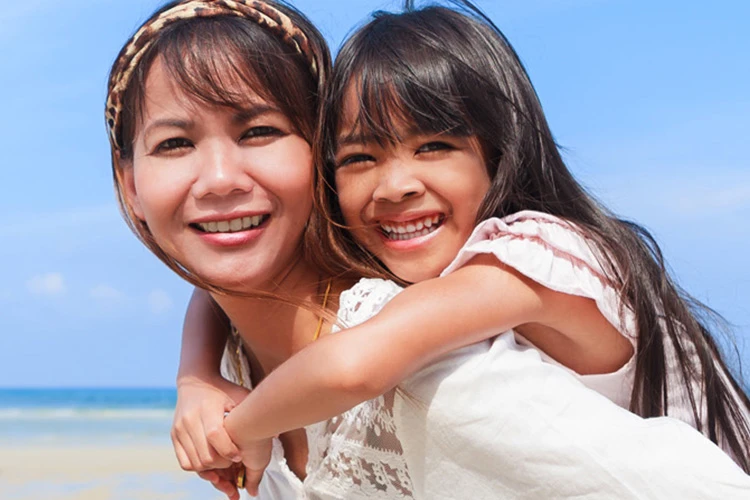 happy mother giving daughter piggyback ride in beach